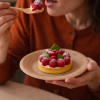 Personne qui mange un tartelette aux framboises dans une assiette à dessert kraft