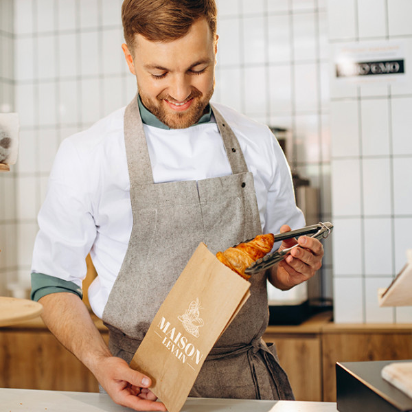 Boulanger emballe croissant dans un sachet kraft personnalisé